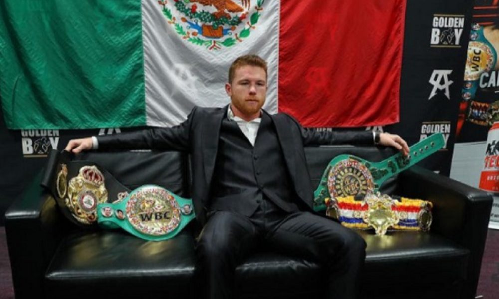 De terno e com a bandeira do México ao fundo, Canelo posa com seus cinturões