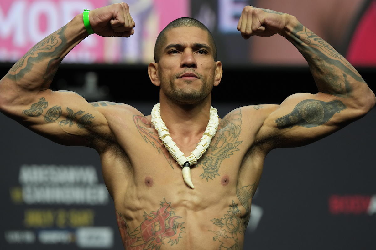 Alex Poatan flexiona os músculos ao subir na balança da pesagem cerimonial do UFC 276.