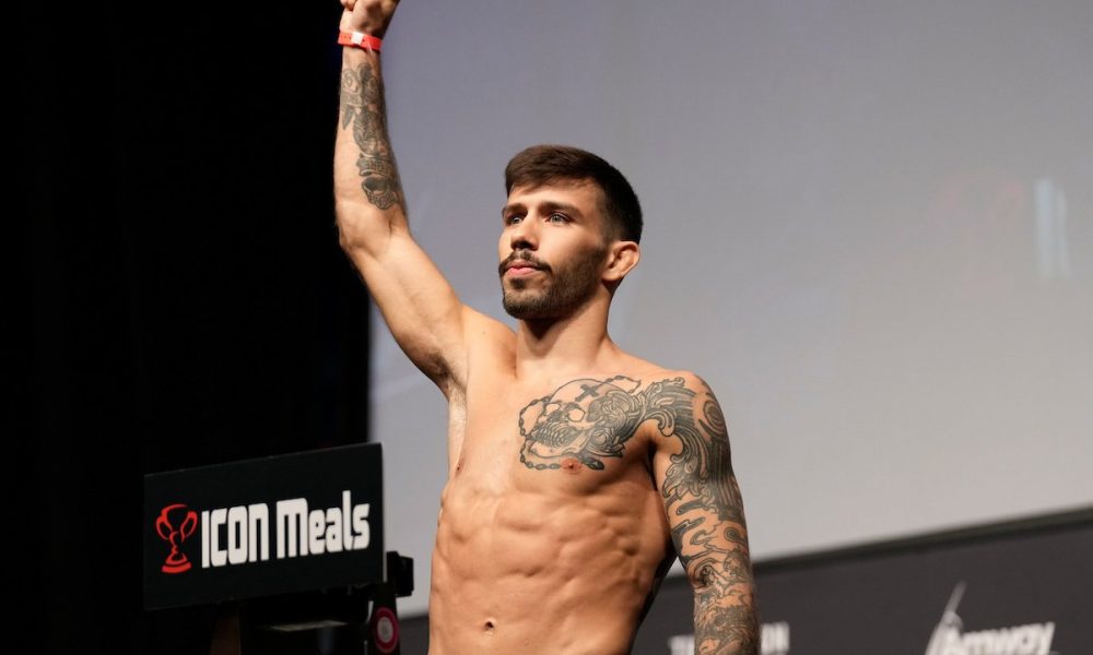 Com o braço direito erguido e punho cerrado, Matheus Nicolau sobe na balança durante pesagem do UFC