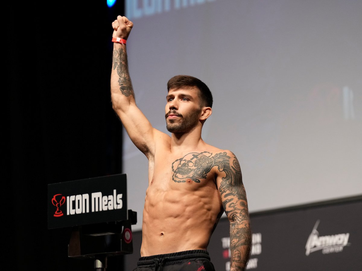 Com o braço direito erguido e punho cerrado, Matheus Nicolau sobe na balança durante pesagem do UFC